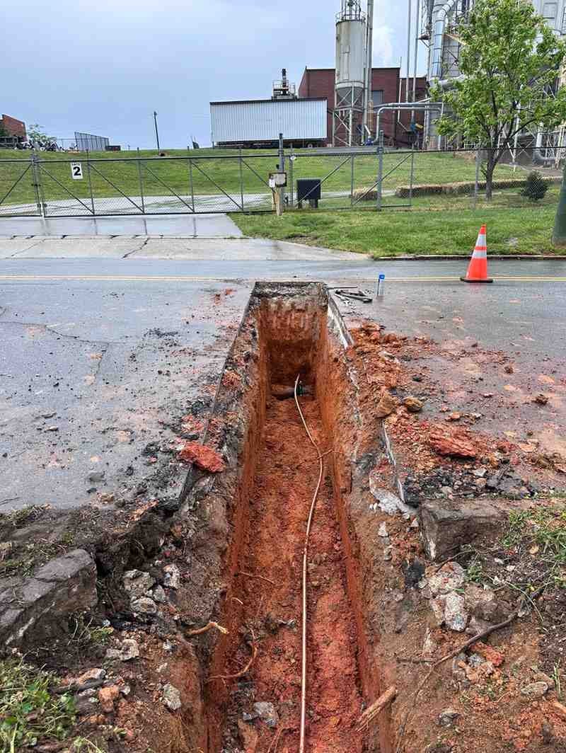 Two construction workers, one in an excavator and another watching from a trench, prepare a new home site.