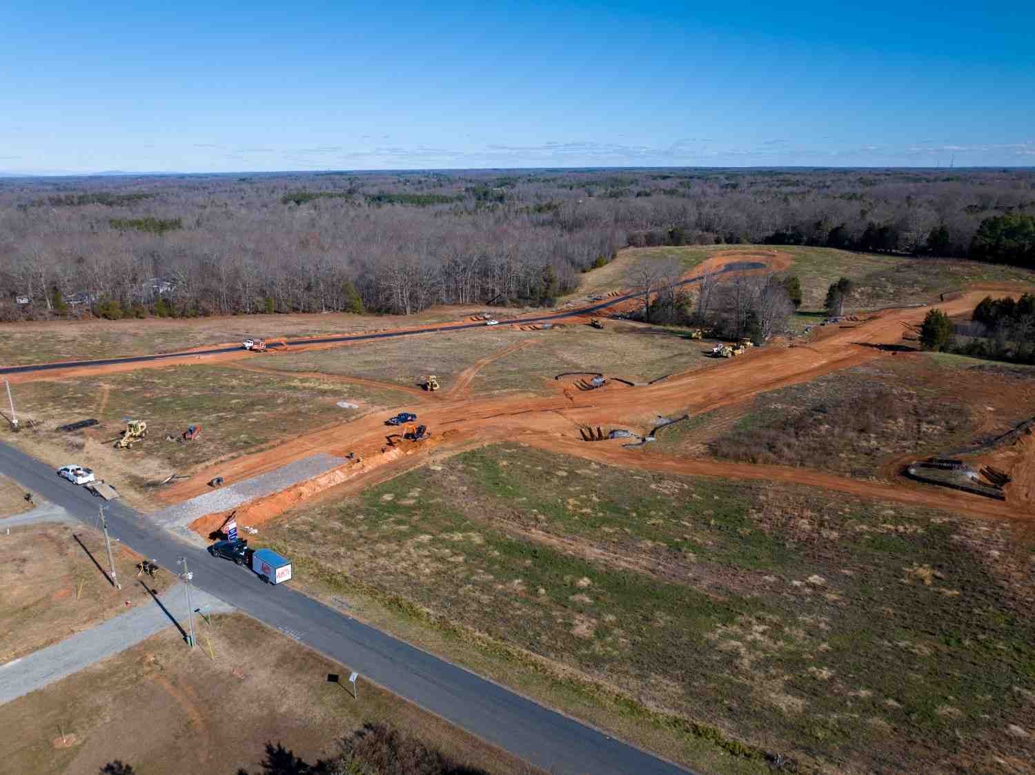 Aerial view of a sprawling construction site with red dirt roads and heavy machinery amidst wooded land.