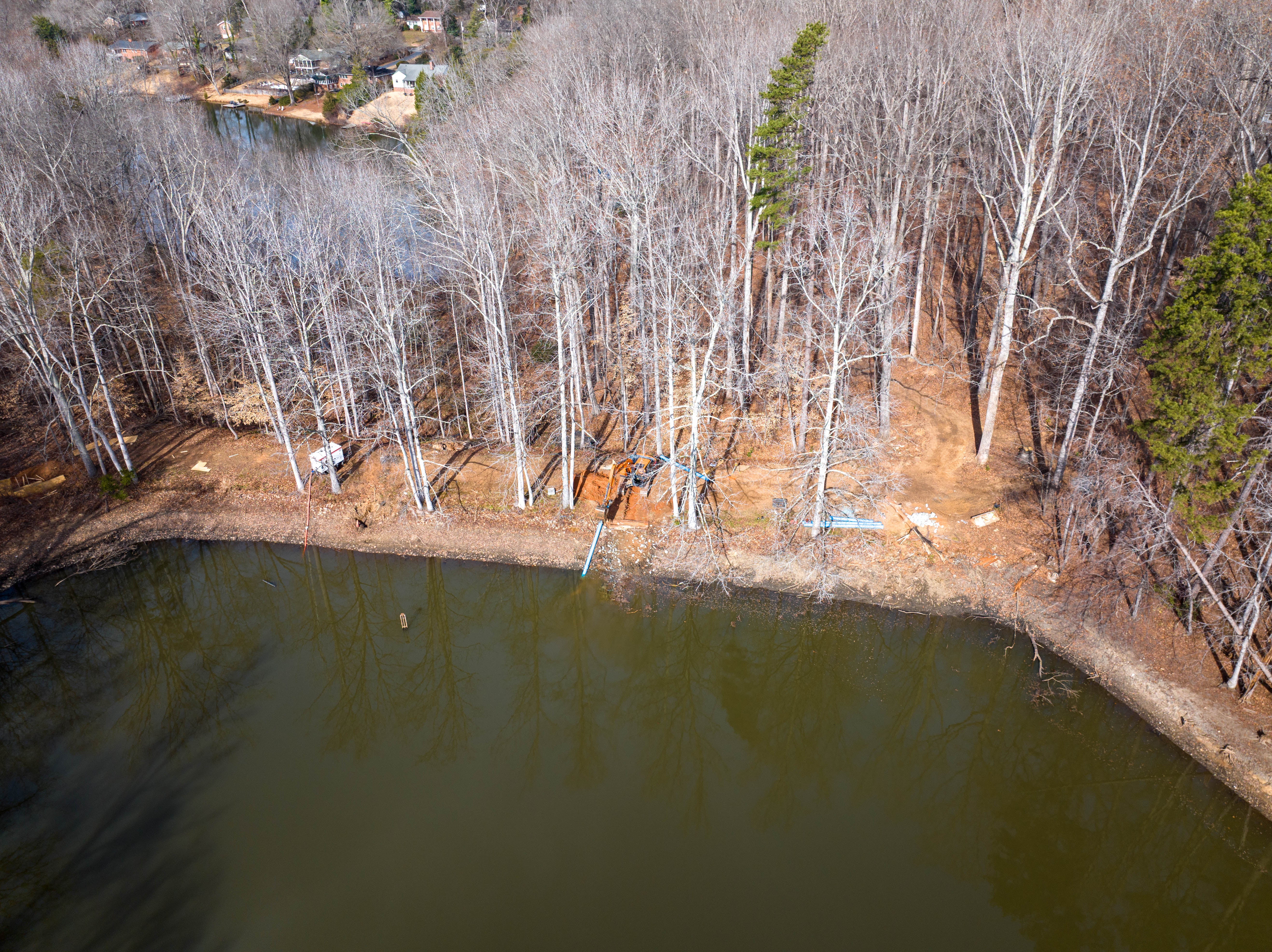 Worksite with excavators digging a trench, a man on a skid steer, and long black pipes on red dirt.