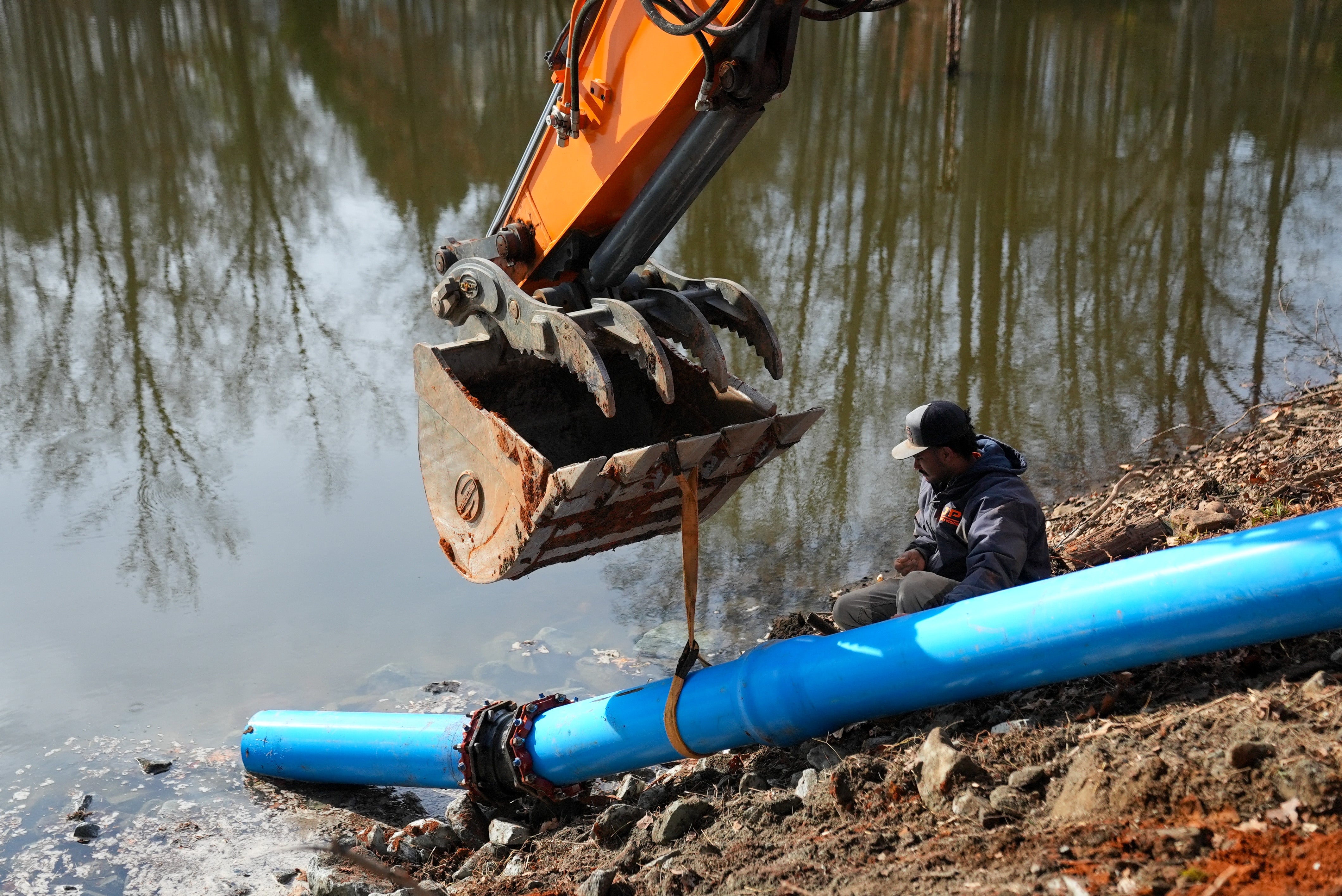 Overhead drone shot of construction workers in a trench and an excavator next to a blue pickup truck.