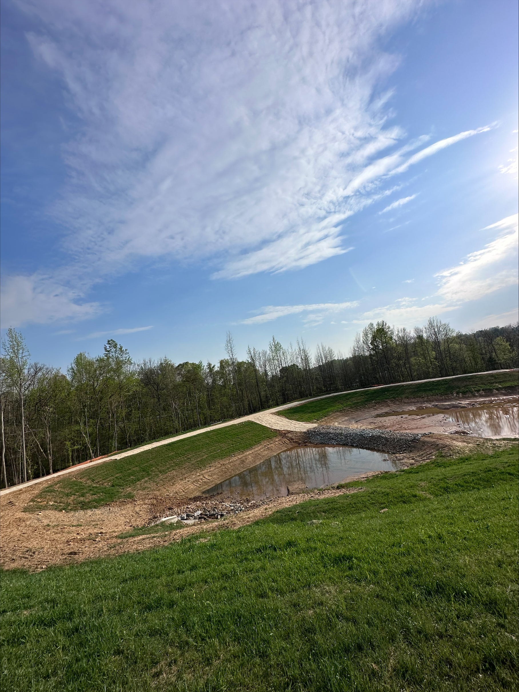 A long, deep trench dug in reddish-brown dirt with a dark pipe laid inside. Construction workers are visible in the background.