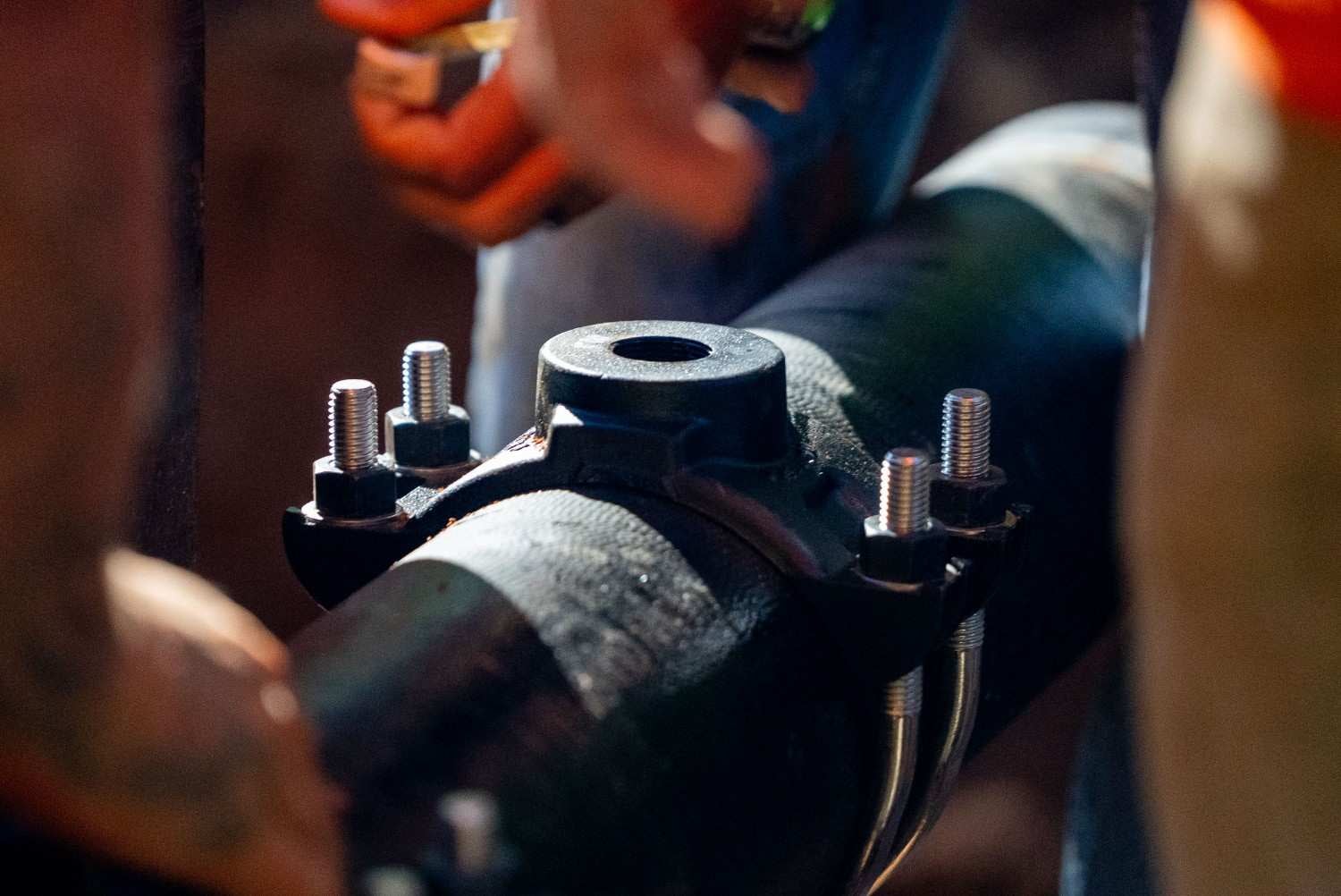 Close-up of a dark pipe with a secured black clamp and stainless steel bolts and nuts.