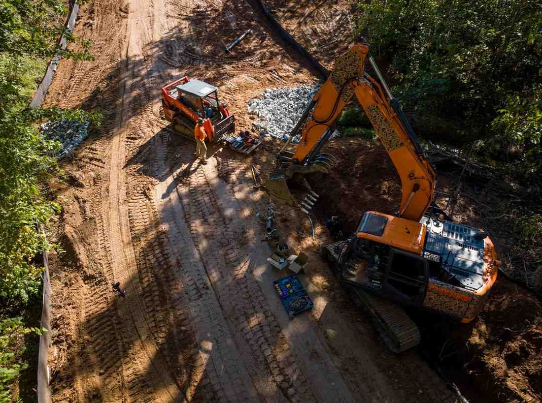 Aerial view of an orange excavator and small skid-steer loader on a dirt construction site with two workers.