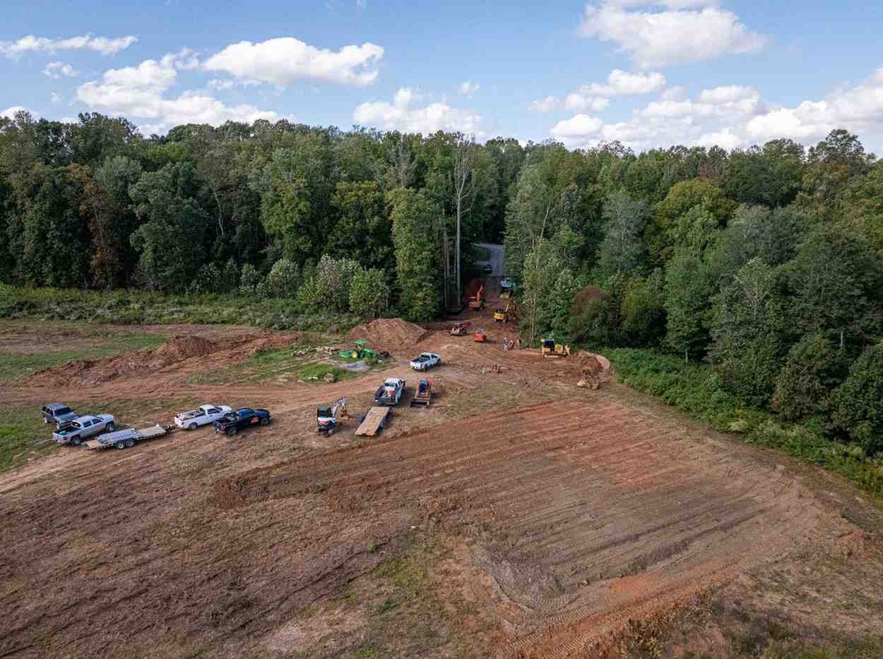 Aerial view of a construction site with heavy machinery, vehicles, and cleared dirt areas next to a dense forest.